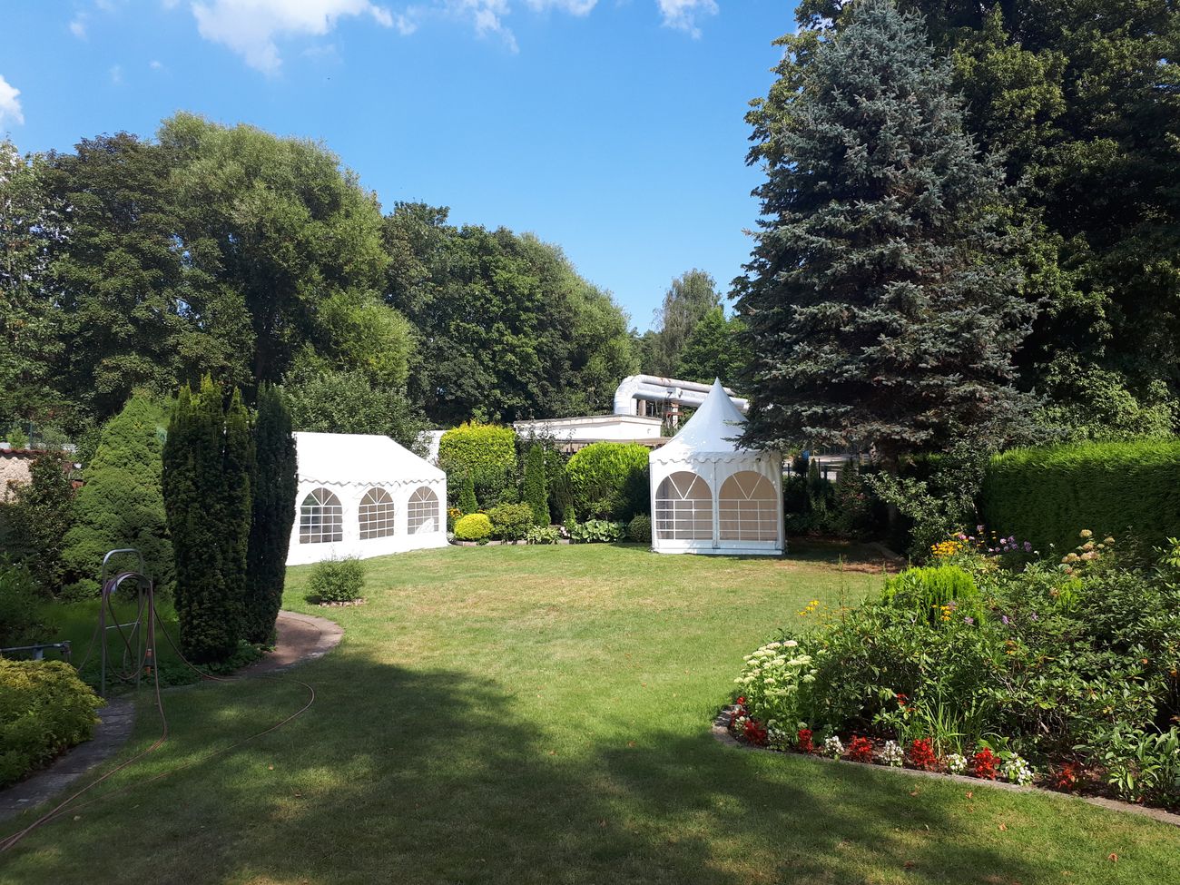 großer Garten mit gepflegtem Rasen und Blumenbeeten mit 2 weißen Zelten