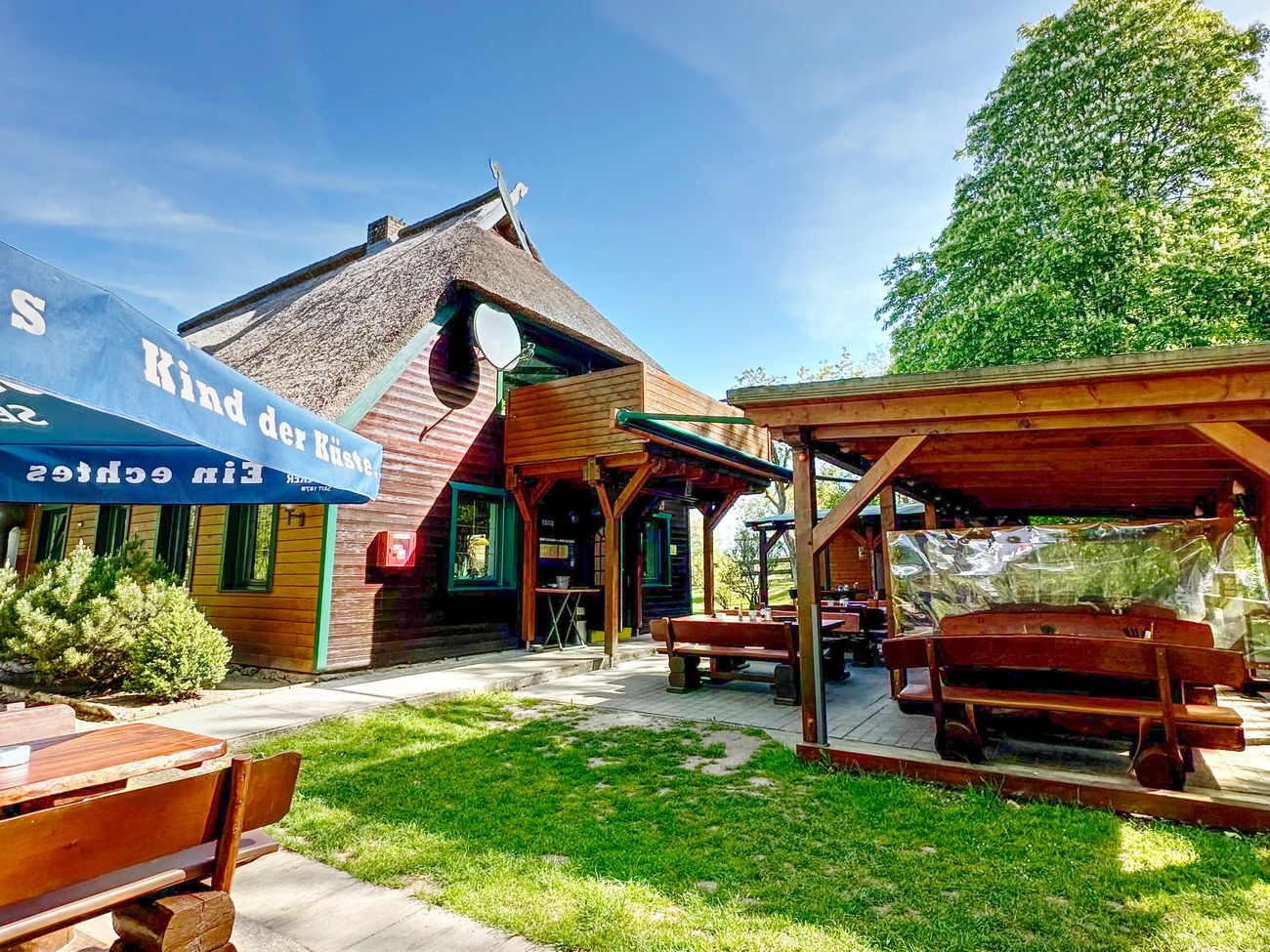 Außenansicht der Gaststätte mit Holzfassade und Reetdach davor überdachte Sitzplätze