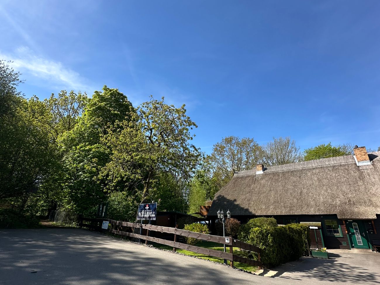 Reetdachhaus am Waldrand mit Straße und Parkplatz vorm Eingang.