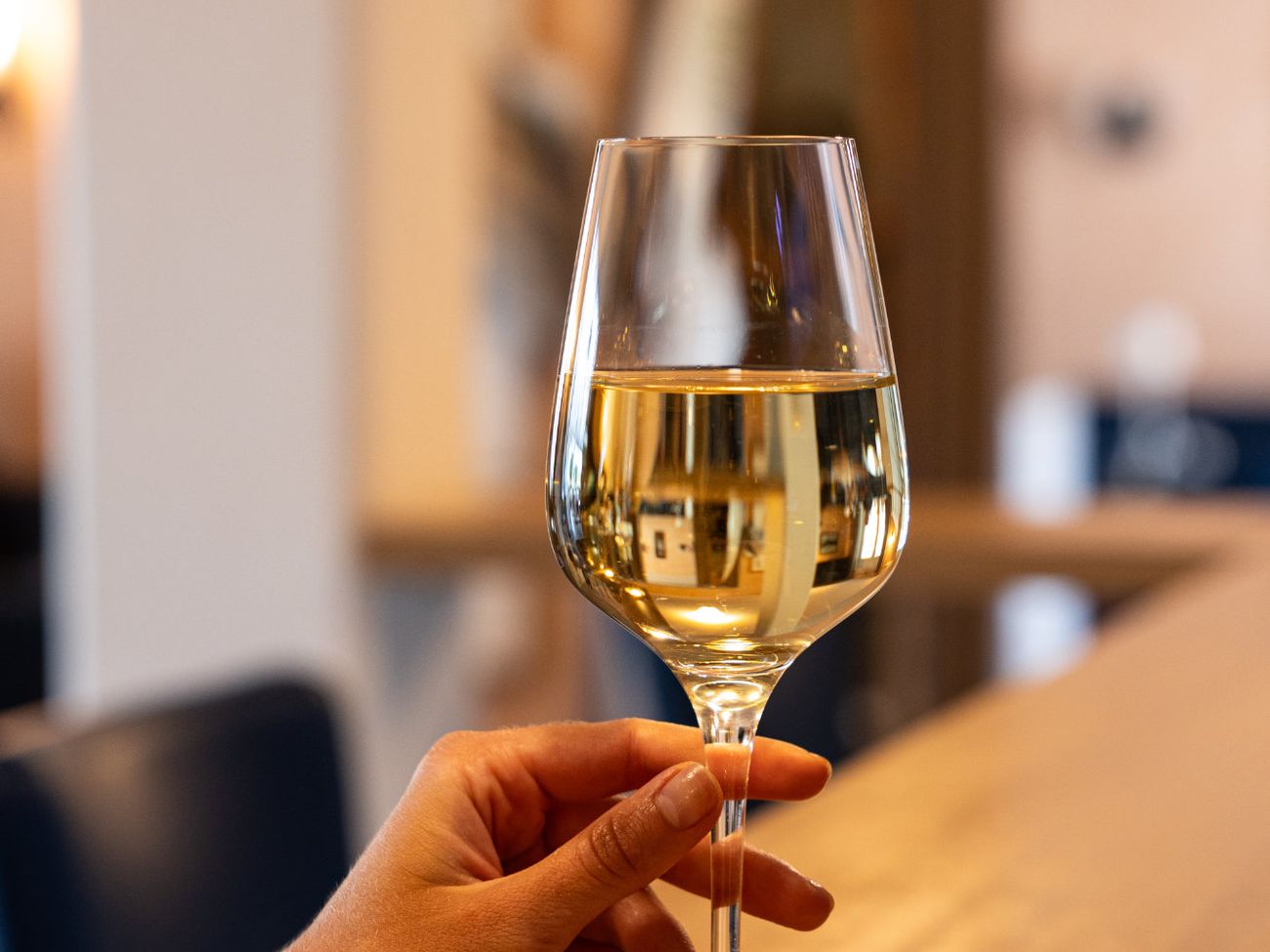 Eine Hand hält ein gefülltes Weißweinglas