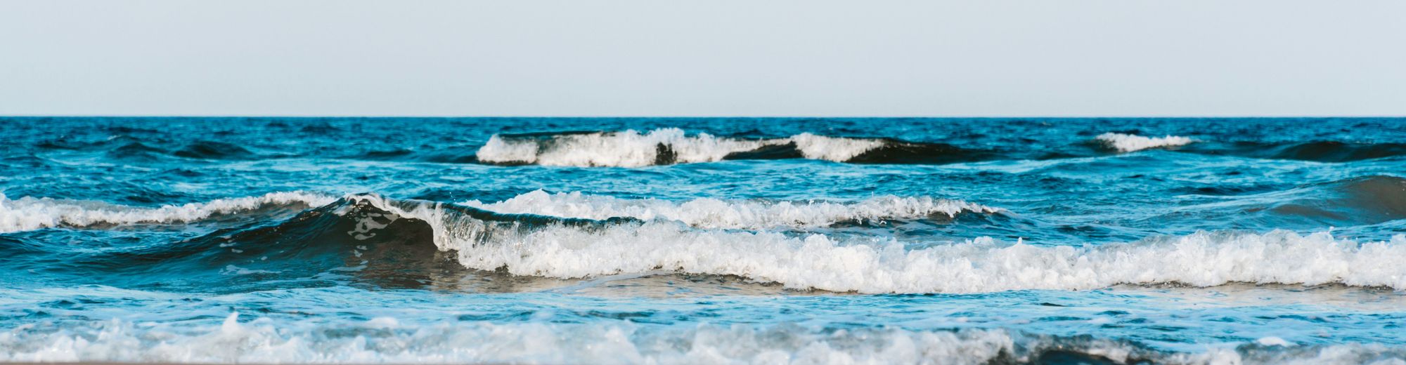 blaue Wellen mit weißen Kronen schwappen auf den Sand