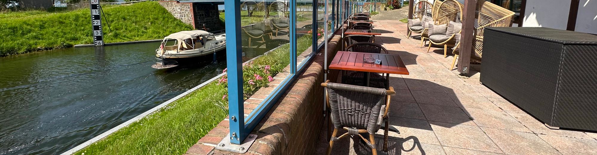 Tischchen auf der Terrasse des Lenzer Krugs direkt am Lenzer Kanal gelegen, auf dem ein Schiff vorbeifährt