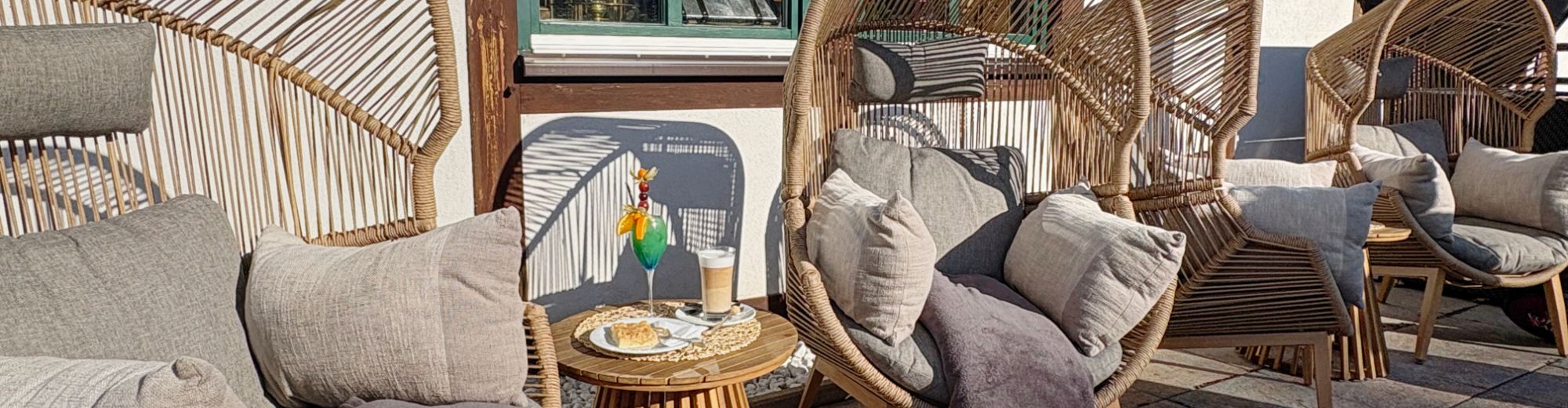 große gemütliche Korbsessel mit Kissen und Decken auf einer Terrasse aufgereiht