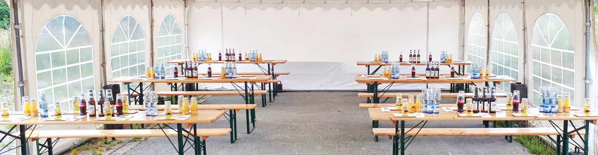 großes, weißes Zelt mit Biertischen auf denen Getränke stehen