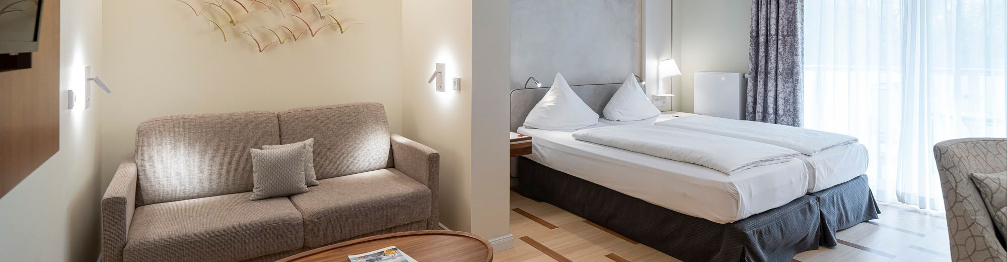 geräumiges Doppelzimmer in hellen Grautönen mit dunklem Holz.