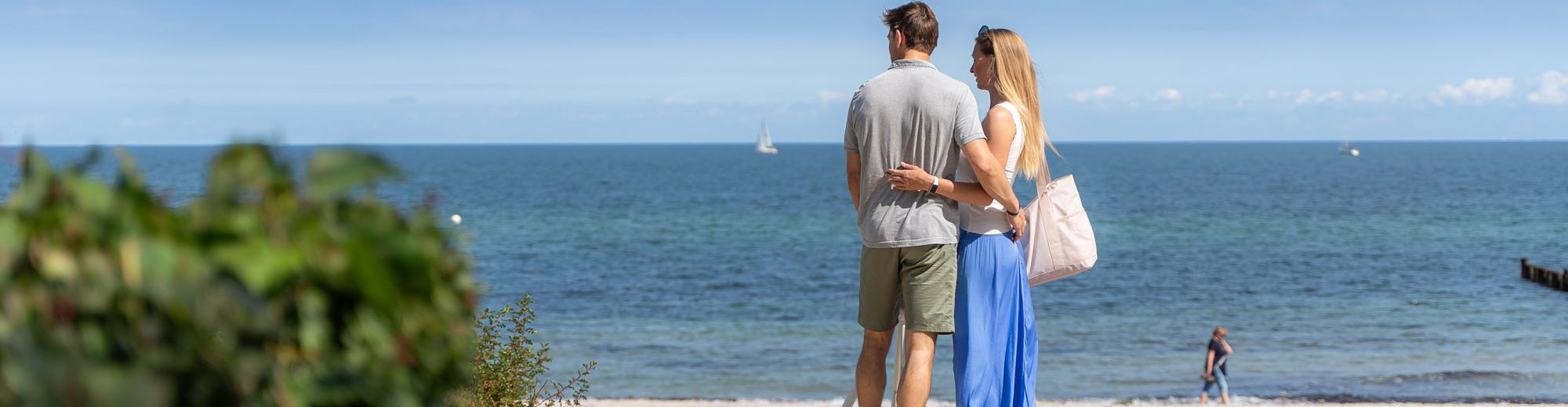 2 Personen stehen auf der Strandpromenade und blicken auf Sandstrand und Meer
