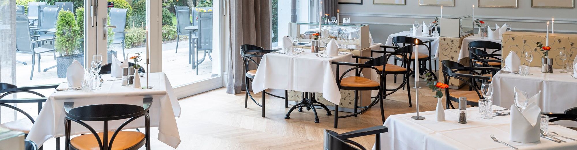 Restaurant mit gedeckten Tischen, bodentiefen Fenstern und Blick auf die Terrasse