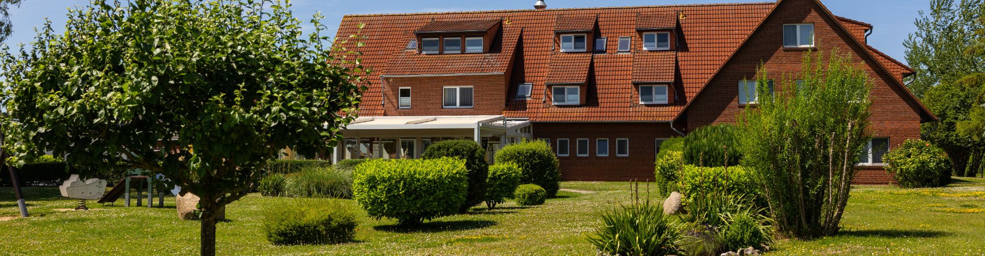 Gepflegter Garten mit runden Büschen, im Hintergrund das Hotel