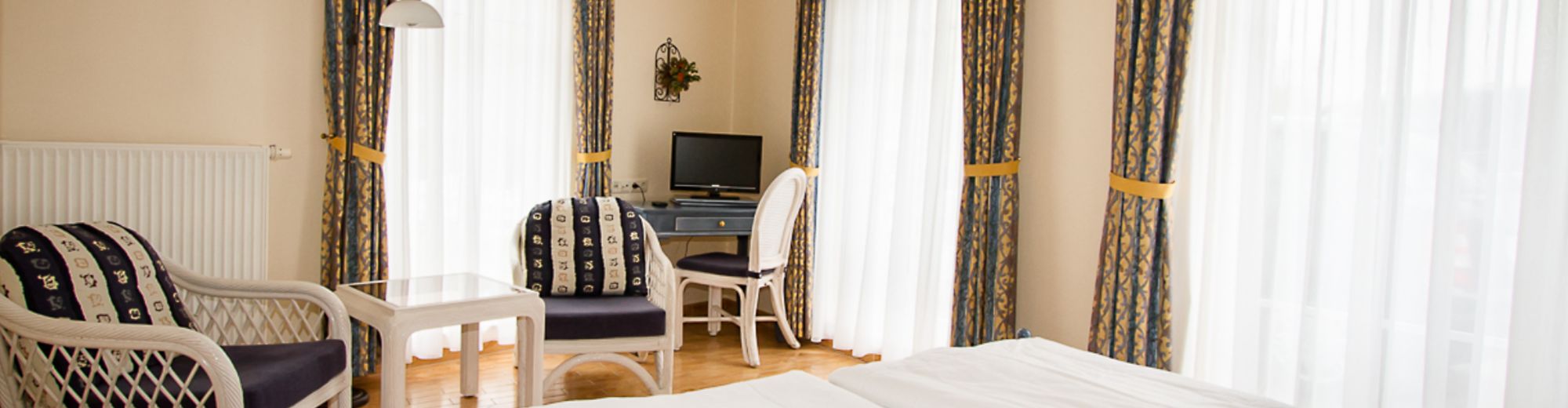 Lichtdurchflutetes Hotelzimmer mit Doppelbett und weißem Korbmobiliar