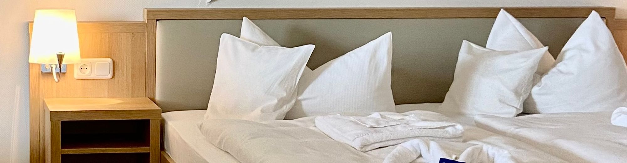 Doppelbett in einem Hotelzimmer mit weißer Bettwäsche und weißen Handtüchern