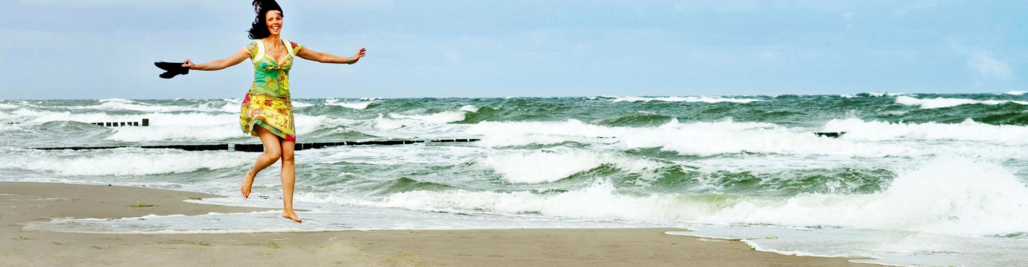Frau läuft über den Strand, ihre Schuhe in der Hand