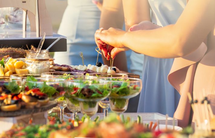 Sommerliches Buffet im Freien mit Gästen, die sich ihre Teller füllen