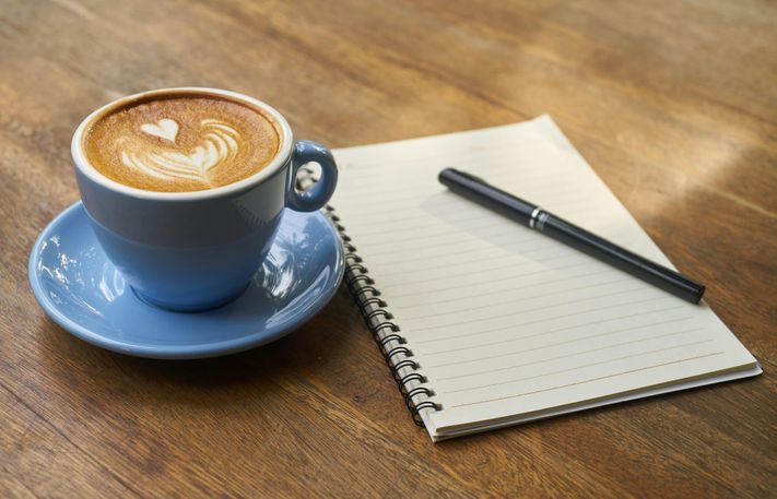 Nahaufnahme Kaffeetasse und Notizblock auf Holzoberfläche liegend
