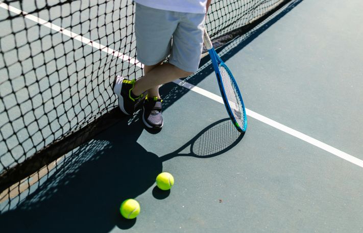 Person steht an einem Tennisnetz mit Tennisschläger