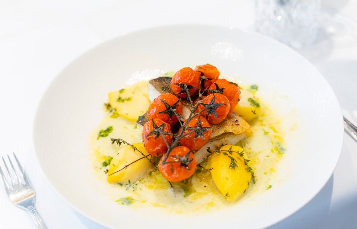 hübsch angerichtete Hauptspeise mit Fisch, Kartoffel und geschmorten Tomaten.