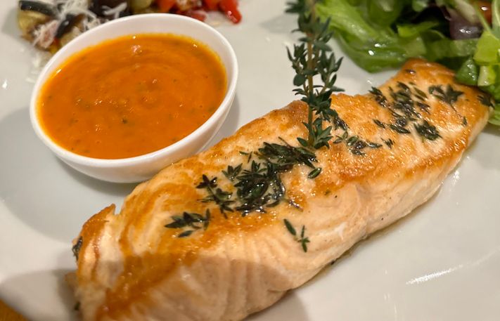 Fischgericht mit Gemüsebeilage und Salatbouquet auf gedecktem Tisch serviert