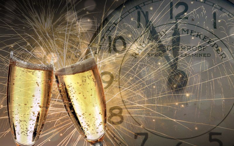 2 gefüllte Sektgläser vor einer Uhr und Feuerwerk